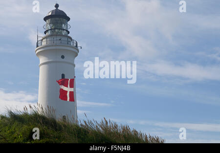 Un drapeau danois flotte fièrement à côté d'un grand vieux phare traditionnel qui se dresse majestueusement sur la côte dans plus de voit. Banque D'Images