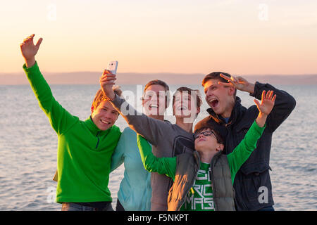 Groupe de jeunes heureux de prendre un avec un blanc selfies smart phone en face d'un lac Banque D'Images