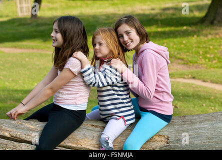 Trois jeunes filles s'asseoir à califourchon sur un journal de lecture faire semblant. L'sont évidemment des amis proches et sont heureux d'être ensemble. Banque D'Images