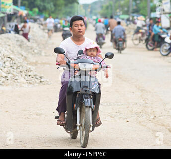 Homme conduisant une moto tout en tenant un bébé dans le canton de Labutta, Division de l'Ayeyarwady du Myanmar. Banque D'Images