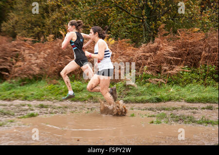 Jeune femme blonde runner enduite dans la pluie et la boue face à éléments en course cross-country avec pelouse de silencieux aux pieds Banque D'Images