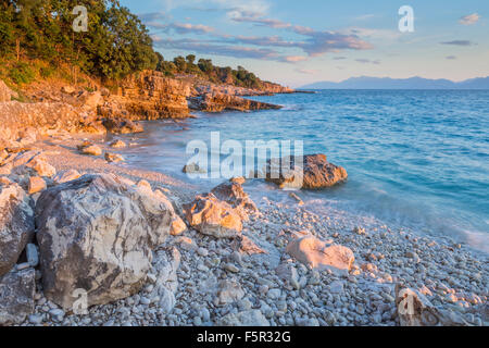 Les cailloux et les rochers sur la plage de Bataria, Kassiopi, Corfou sont éclairés avec la lumière du lever du soleil orange Stong. Banque D'Images