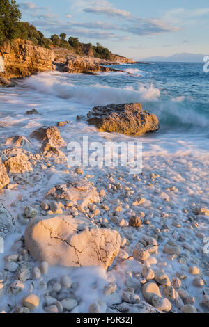 Les cailloux et les rochers sur la plage de Bataria, Kassiopi, Corfou sont éclairés avec la lumière du lever du soleil orange Stong. Banque D'Images