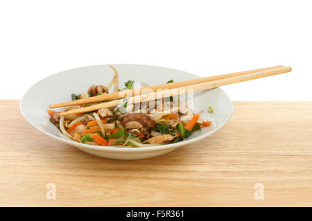 Poulet sauté de légumes abd avec des baguettes dans un bol sur une table en bois Banque D'Images