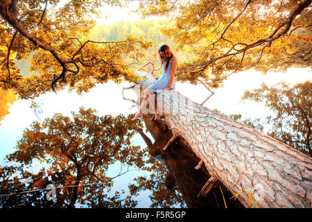 Automne dans la forêt et le lac. Belle jeune fille assise sur l'arbre abattu au-dessus de l'eau. Banque D'Images