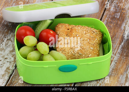 École en santé boîte à lunch contenant rouleau de grains entiers avec du fromage et de la laitue, les raisins, les tomates cerises et les bâtonnets de concombre Banque D'Images