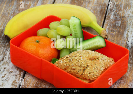 École en santé boîte à lunch contenant rouleau de grains entiers avec du fromage et de la laitue, le concombre bâtonnets, raisin, mandarine et la banane Banque D'Images