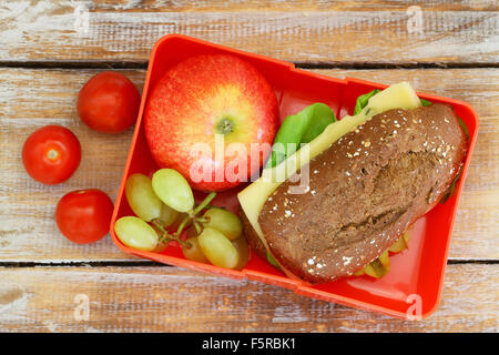 École en santé boîte à lunch contenant rouleau de grains entiers avec du fromage et de la laitue, tomates cerise, pomme rouge et le raisin Banque D'Images