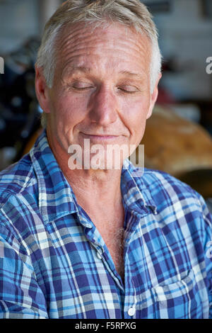 Portrait d'un homme d'âge mûr avec ses yeux fermés en contemplant sa vie heureuse dans son hangar Banque D'Images
