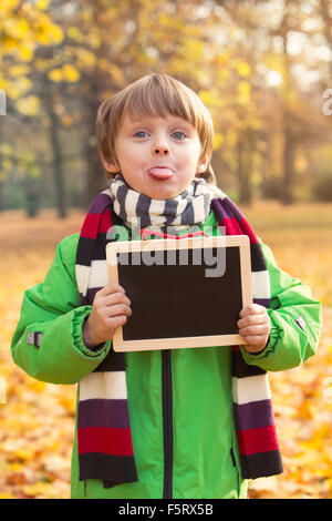 Garçon dans le parc à l'automne la tenue d'un tableau noir et en tirant sa langue Banque D'Images