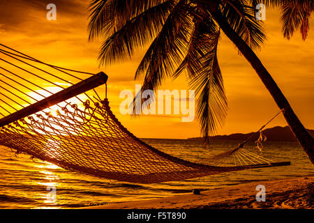 Silhouette d'hamac et palmiers sur une plage tropicale au coucher du soleil Banque D'Images