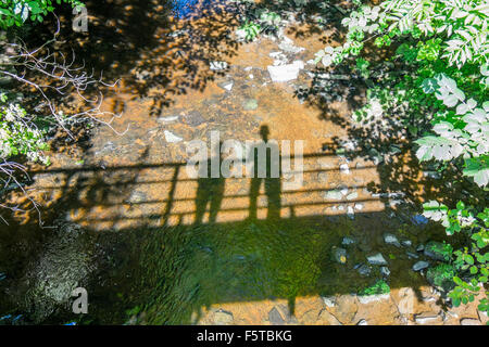 L'ombre de deux personnes debout sur un pont qui se reflète dans la rivière, Banque D'Images