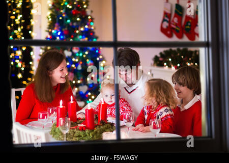 Grande famille avec trois enfants célébrer Noël à la maison. Dîner de fête à cheminée et arbre de Noël. Parent et enfant de manger Banque D'Images