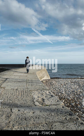 Teenage boy walking le long de la mur du port de Cobb à Lyme Regis, dans le Dorset, Angleterre, RU Banque D'Images