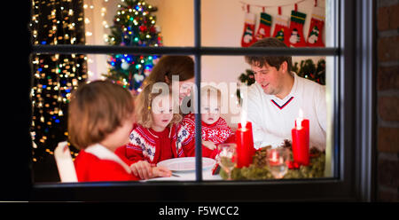 Grande famille avec trois enfants célébrer Noël à la maison. Dîner de fête à cheminée et arbre de Noël. Parent et enfant de manger Banque D'Images