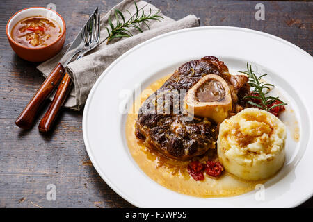 Osso Buco de veau préparée avec des tomates et de la purée de pommes de terre sur la plaque blanche sur fond de bois Banque D'Images