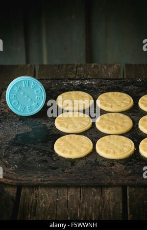 Sablés cuits avant d'être pour le faire cuire, avec timbre bleu avec l'inscription faite maison. Sur noir planche à découper. Rustique foncé Banque D'Images