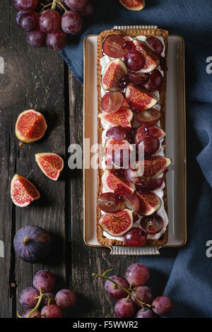 Tarte rectangulaire rouge avec des raisins, figues et à la crème fouettée dans la plaque en céramique blanche ancienne table en bois avec dessus textile bleu Banque D'Images