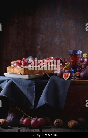 Tarte rectangulaire rouge avec des raisins, figues, noix et crème fouettée dans la plaque en céramique blanche sur la poitrine en bois plus vieux woode Banque D'Images
