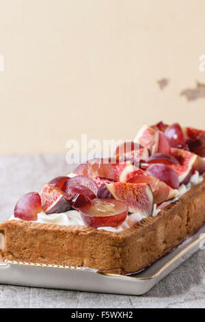 Close up de tarte rectangulaire rouge avec raisins, figues et à la crème fouettée dans la plaque en céramique blanche sur table en bois blanc. Banque D'Images