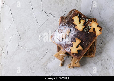 Shortbread cookies de Noël pour les tasses de sucre en poudre sur petite planche à découper en bois gris sur surface plâtrée. Formes Cookies Banque D'Images