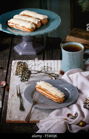 Ancienne table de Noël en bois avec des éclairs à la crème au beurre et tasse de thé chaud, décorer pour Noël étoile, arbre et vintage books. Banque D'Images