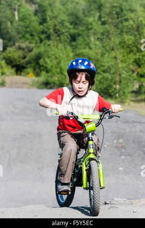 Caucasien enfant, garçon de 9 ans, équitation, vélo d'enfant vers viewer sur piste sale, tout en portant un casque. Pleine longueur. L'ensoleillement. Banque D'Images