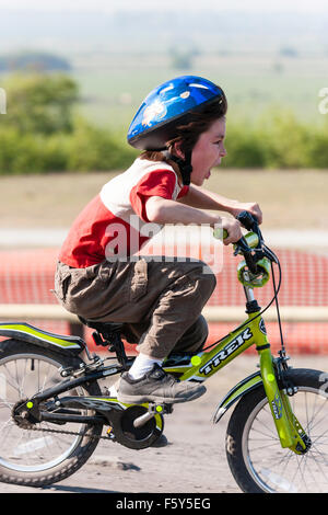 Vue latérale de Blancs 9 ans enfant, garçon, équitation, bicyclette d'enfant en vitesse avec enthousiaste de l'expression du visage. Le port de casque bleu et tee-shirt. Banque D'Images