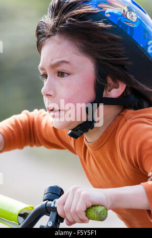L'Angleterre. Caucasien enfant, garçon de 9 ans. Équitation vélo à vitesse avec blurrey arrière-plan. Expression du visage, déterminé la concentration. Banque D'Images