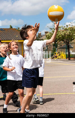 Enfant, garçon de race blanche, 7 à 9 ans. À l'extérieur à l'école sports le jour. Sauter de haut et basket ball lancer en l'air avec les deux mains. Banque D'Images
