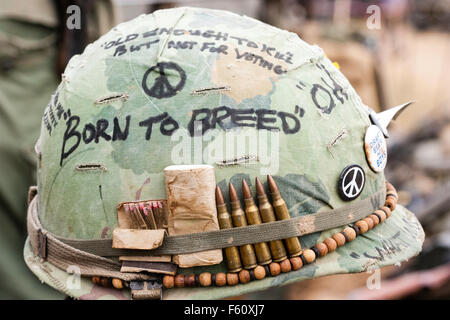 Vietnam Re-enactment. GI américain casque, avec 'Born to Race' écrit sur le côté, avec les signes de paix, cartouches bloqué en bande autour de la jante. Banque D'Images