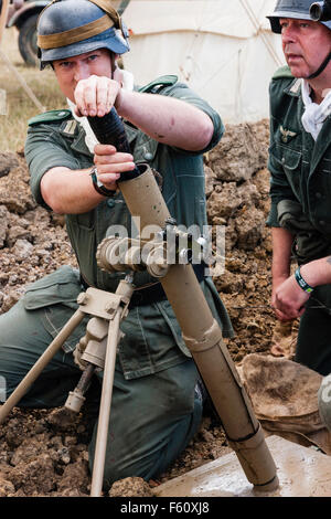 Seconde guerre mondiale re-enactment. Deux hommes de l'équipe de mortier dans de petites pirogues. Un soldat 8 cm de chargement d'obus de mortier mortier de tranchée dans la lumière. Close up. Banque D'Images