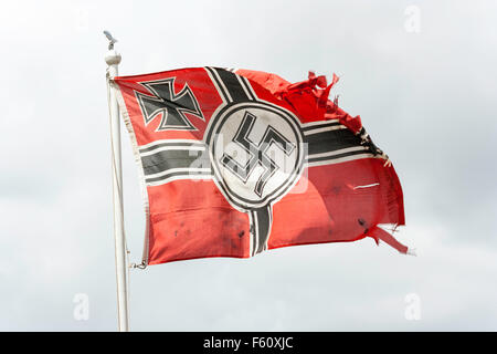 La seconde guerre mondiale remise en vigueur. Guerre déchirée Wehrmacht allemande drapeau avec croix de fer et croix gammée nazie, en volant au-dessus d'un mât contre ciel gris orageux. Banque D'Images