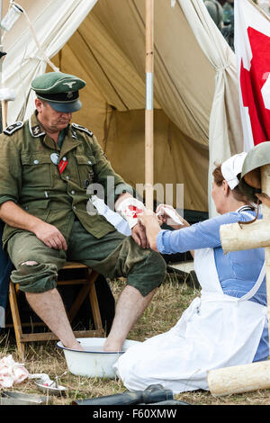 La seconde guerre mondiale remise en vigueur. Officier allemand ayant un bain de pieds et d'être traité pour une blessure au bras inférieur de bataille clearing station par infirmière. Banque D'Images