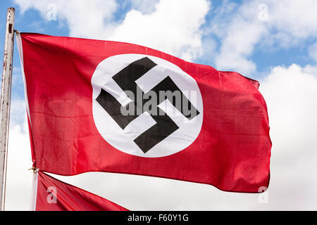 La seconde guerre mondiale remise en vigueur. L'allemand rouge, blanc et noir du drapeau à croix gammée nazie. Palpitations dans breeze contre ciel bleu avec des nuages blancs. Banque D'Images