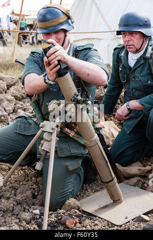 Seconde guerre mondiale re-enactment. Deux hommes de l'équipe de mortier dans de petites pirogues. Un soldat 8 cm de chargement d'obus de mortier mortier de tranchée dans la lumière. Close up. Banque D'Images