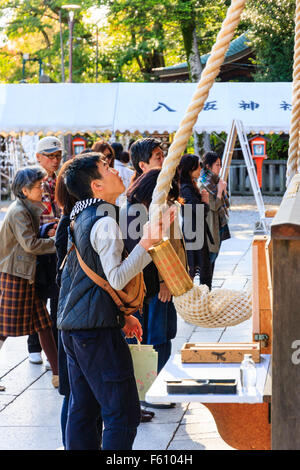 Young man, vue de côté, la détention et la cloche qui sonne corde avec les deux mains tout en priant devant le hall de l'Gion-Zukuri Yasaka à Kyoto. Banque D'Images