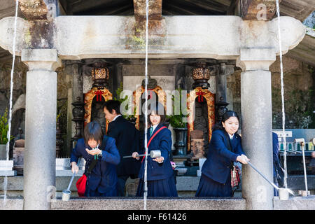 Le Japon, Kyoto, temple Kiyomizu dera, 3 écolières japonaise prenant l'eau à partir de la célèbre Otowa-no-taki, 'Sound of feathers' cascade Banque D'Images