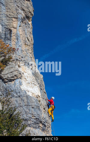 Rock climber mature en jaune et rouge sur la falaise avec ciel bleu Banque D'Images