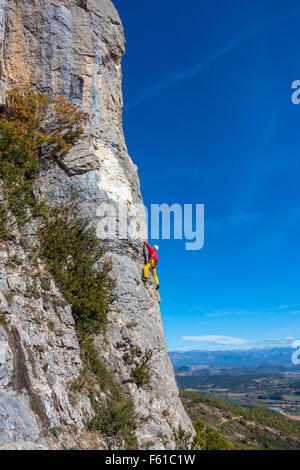 Rock climber mature en jaune et rouge sur la falaise avec ciel bleu Banque D'Images