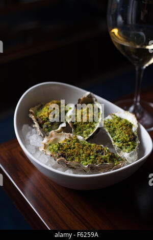 Vue en angle de l'huîtres Rockefeller sur la glace sur le coin d'une table avec un verre de vin blanc à l'arrière-plan. Banque D'Images