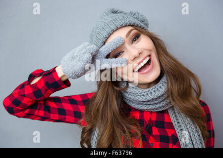 Portrait d'un drôle de laughing woman montrant deux doigts signer sur fond gris Banque D'Images