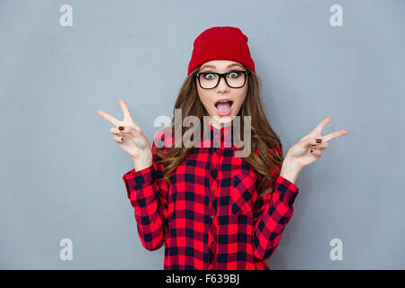 Portrait d'une femme à la mode joyeux montrant deux doigts signer sur fond gris Banque D'Images