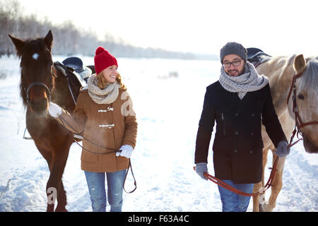 Jeune couple heureux avec les chevaux marcher en hiver jour Banque D'Images