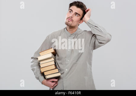 Young attractive smart bel homme en chemise grise penser et holding books Banque D'Images