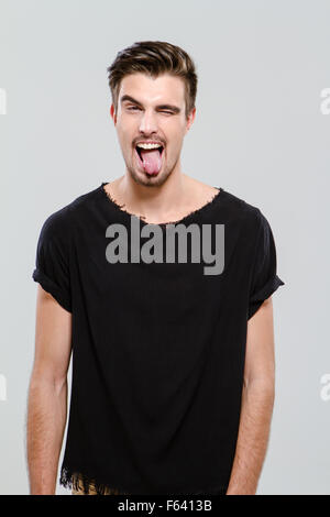 Drôle jeune beau gars en t-shirt noir avec un clin et qui sort sa langue Banque D'Images