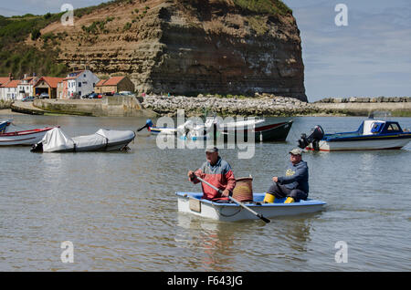 Journée ensoleillée, 2 pêcheurs rament à la rive dans un petit bateau avec leur crochet de pêche - port de mer, Staithes' village, North Yorkshire, UK. Banque D'Images