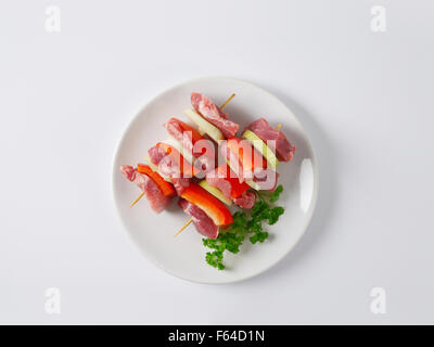 Deux brochettes de porc cru avec des viandes et des légumes sur plaque blanche Banque D'Images