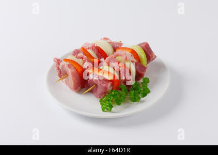 Deux brochettes de porc cru avec des viandes et des légumes sur plaque blanche Banque D'Images