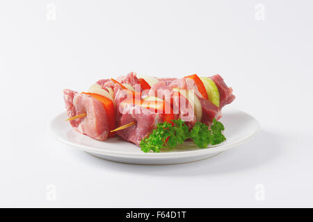 Deux brochettes de porc cru avec des viandes et des légumes sur plaque blanche Banque D'Images